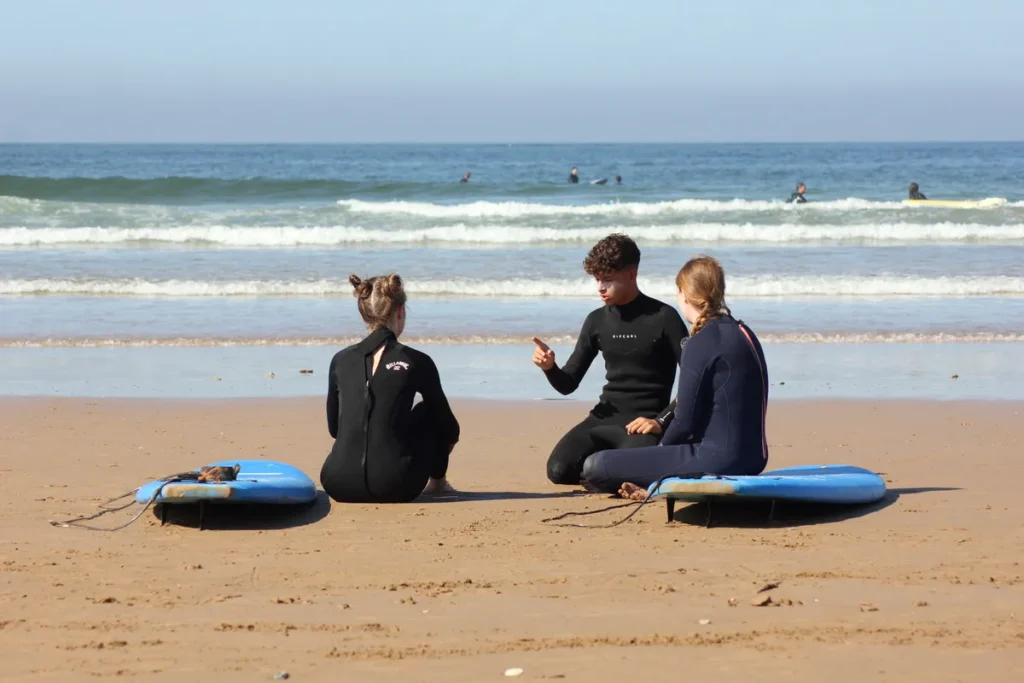 Istruttore di surf che spiega le basi a due allievi nel nostro surf camp all inclusive in Marocco